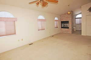 Unfurnished living room featuring a brick fireplace, vaulted ceiling, ceiling fan, and carpet flooring