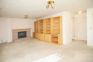 Unfurnished living room featuring a brick fireplace, light colored carpet, and a textured ceiling