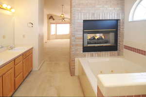 Bathroom featuring vanity, tiled tub, a fireplace, and ceiling fan