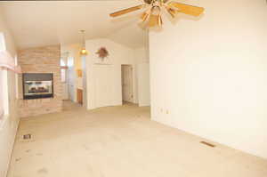 Unfurnished living room with vaulted ceiling, a brick fireplace, carpet floors, and ceiling fan