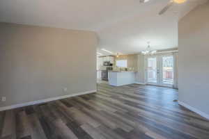 Unfurnished living room featuring ceiling fan with notable chandelier, lofted ceiling, sink, dark hardwood / wood-style flooring, and french doors