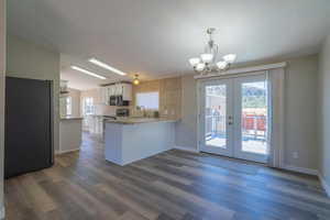 Kitchen with dark wood-type flooring, french doors, stainless steel range with electric stovetop, kitchen peninsula, and pendant lighting