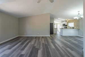 Unfurnished living room with dark hardwood / wood-style flooring, sink, and ceiling fan with notable chandelier