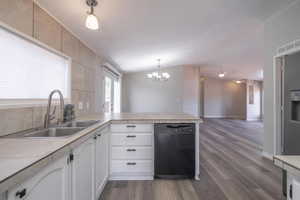 Kitchen with sink, hanging light fixtures, black dishwasher, white cabinets, and kitchen peninsula