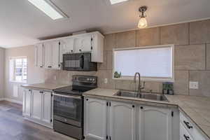 Kitchen featuring electric stove, white cabinetry, and sink