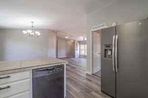 Kitchen with decorative light fixtures, black dishwasher, white cabinets, stainless steel fridge with ice dispenser, and light hardwood / wood-style flooring