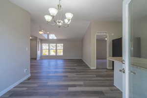 Unfurnished dining area with dark wood-type flooring, vaulted ceiling, and ceiling fan with notable chandelier