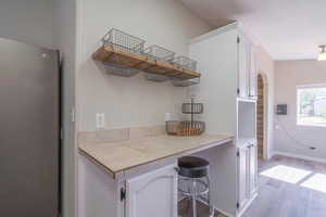 Kitchen with stainless steel refrigerator, white cabinetry, a kitchen bar, tile countertops, and light wood-type flooring