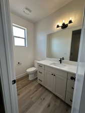 Bathroom with visible vents, baseboards, toilet, wood finished floors, and vanity
