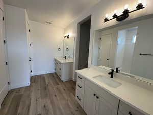 Full bathroom featuring a sink, visible vents, two vanities, and wood finished floors