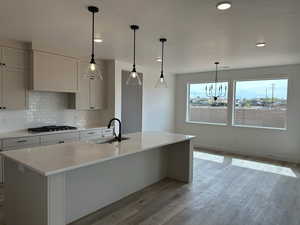 Kitchen featuring a sink, tasteful backsplash, gas stovetop, light wood finished floors, and light countertops