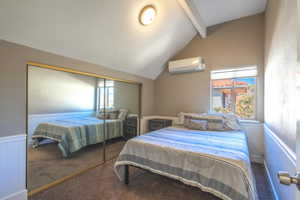 Bedroom featuring vaulted ceiling with beams, dark carpet, multiple windows, and an AC wall unit