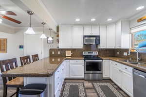 Kitchen with appliances with stainless steel finishes, a breakfast bar, decorative light fixtures, white cabinets, and kitchen peninsula