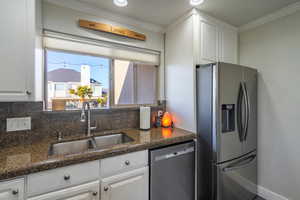 Kitchen with sink, white cabinetry, ornamental molding, appliances with stainless steel finishes, and backsplash