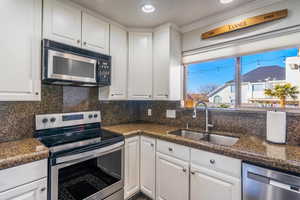 Kitchen featuring sink, white cabinetry, stainless steel appliances, tasteful backsplash, and ornamental molding