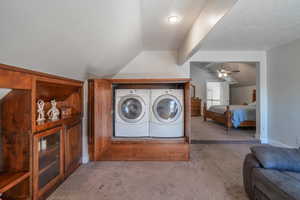 Laundry room with ceiling fan, separate washer and dryer, light colored carpet, and a textured ceiling