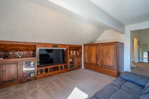 Living room featuring built in shelves, vaulted ceiling, and light colored carpet