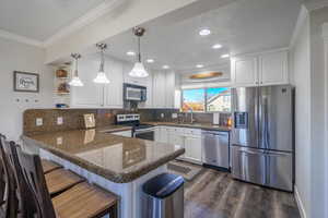 Kitchen with a breakfast bar, white cabinetry, stainless steel appliances, ornamental molding, and kitchen peninsula