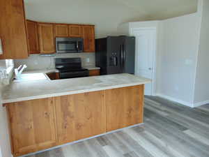 Kitchen with light wood-type flooring, black appliances, sink, and kitchen peninsula