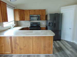 Kitchen featuring kitchen peninsula, black appliances, wood-type flooring, and sink