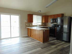 Kitchen with vaulted ceiling, light hardwood / wood-style flooring, kitchen peninsula, and stainless steel appliances