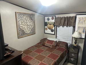 Bedroom with crown molding, lofted ceiling, and a textured ceiling