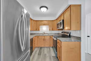 Kitchen featuring sink, stone countertops, light brown cabinets, appliances with stainless steel finishes, and light hardwood / wood-style floors