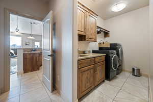 Laundry area featuring light tile patterned flooring, sink, cabinets, a textured ceiling, and washer and clothes dryer