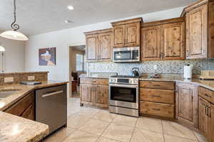 Kitchen with light stone counters, appliances with stainless steel finishes, decorative light fixtures, and tasteful backsplash