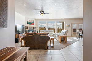 Living room featuring light tile patterned flooring, french doors, a textured ceiling, ceiling fan, and a fireplace