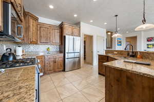 Kitchen featuring sink, stainless steel appliances, light stone counters, decorative backsplash, and decorative light fixtures