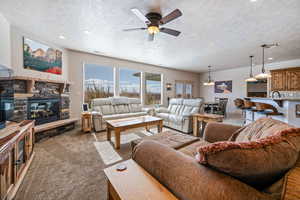 Living room featuring ceiling fan, light colored carpet, a fireplace, and a textured ceiling