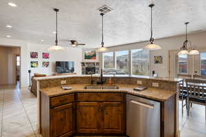 Kitchen featuring sink, dishwasher, a fireplace, an island with sink, and decorative light fixtures