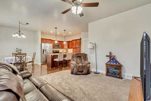 Living room with ceiling fan with notable chandelier and light wood-type flooring