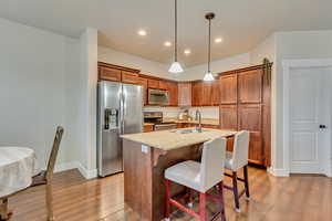 Kitchen featuring pendant lighting, sink, stainless steel appliances, light stone countertops, and a center island with sink