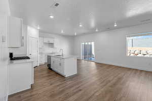 Kitchen with sink, white cabinetry, dishwasher, hardwood / wood-style flooring, and a kitchen island with sink