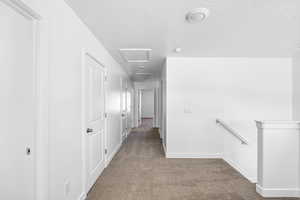 Corridor featuring light colored carpet and a textured ceiling