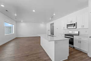 Kitchen featuring stainless steel appliances, white cabinetry, sink, and a kitchen island with sink