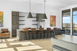 Kitchen with dark brown cabinetry, hanging light fixtures, stainless steel fridge, a kitchen breakfast bar, and a kitchen island with sink