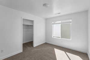 Unfurnished bedroom with a spacious closet, a closet, a textured ceiling, and dark colored carpet