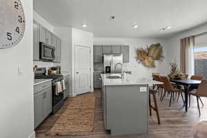 Kitchen with stainless steel appliances, sink, an island with sink, and gray cabinetry