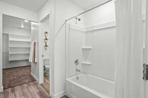 Bathroom with hardwood / wood-style flooring, shower / tub combo with curtain, and toilet