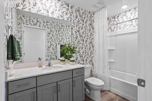 Full bathroom with vanity, wood-type flooring, shower / tub combo with curtain, and toilet