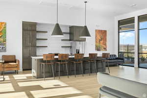 Kitchen with decorative light fixtures, dark brown cabinets, a kitchen breakfast bar, stainless steel fridge, and an island with sink