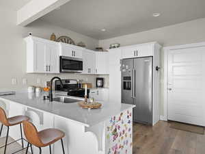 Kitchen featuring stainless steel appliances, white cabinetry, a kitchen breakfast bar, and kitchen peninsula