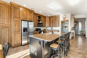 Kitchen featuring sink, a kitchen bar, black appliances, light stone countertops, and a center island with sink