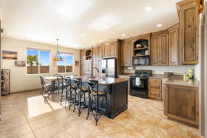 Kitchen featuring pendant lighting, a breakfast bar area, dark stone countertops, black appliances, and an island with sink