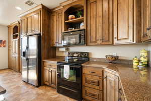 Kitchen featuring dark stone counters, light tile patterned floors, and black appliances