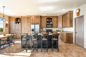 Kitchen featuring hanging light fixtures, a kitchen breakfast bar, light stone counters, black appliances, and an island with sink