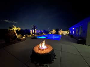 Pool at night with a patio and an outdoor fire pit